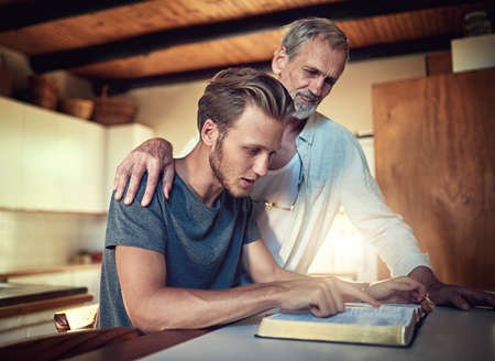 Theyre a family made stronger in faith. Shot of a father and son doing Bible study together at home.の写真素材