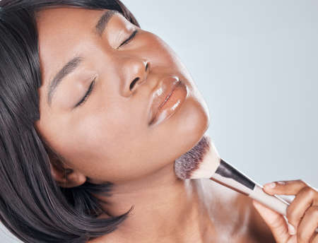 Its not over until youve blended it all in. Studio shot of an attractive young woman using a makeup brush against a grey background.の写真素材