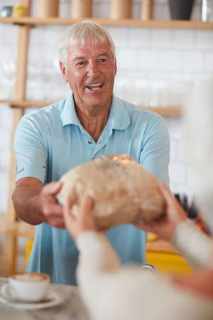 Straight from the oven to you. Shot of a happy senior man serving a customer in a bakery.の写真素材