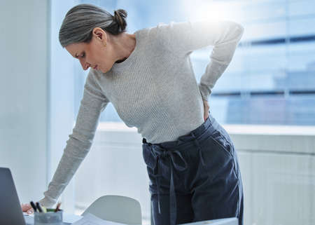 Wheres the chiropractor when you need one. Shot of a mature businesswoman standing alone in the office and suffering from backache.の写真素材