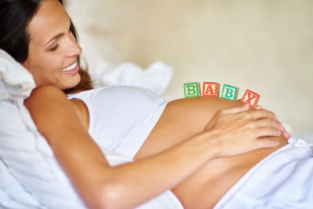 She cant wait to be a mom. Shot of a pregnant woman lying down with wooden baby blocks on her belly.の写真素材