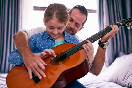 Musical bonding. Cropped shot of a father and daughter playing the guitar together at home.の写真素材