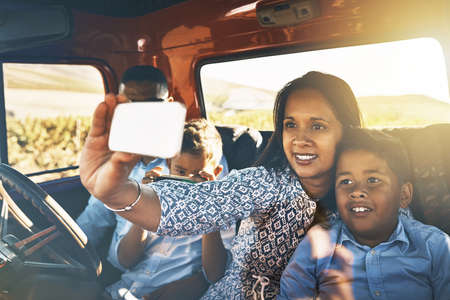 Time for some photos for the memories. Shot of a cheerful young family driving in a red pickup truck on a rural road while taking a self portrait on a cellphone together.の写真素材
