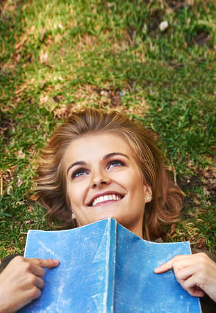Books can really get your mind going. Shot of an attractive young woman reading a book while lying outside on the grass.の写真素材
