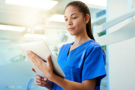 Time for a second opinion. Shot of a young nurse using a tablet while standing inside a clinic.の写真素材
