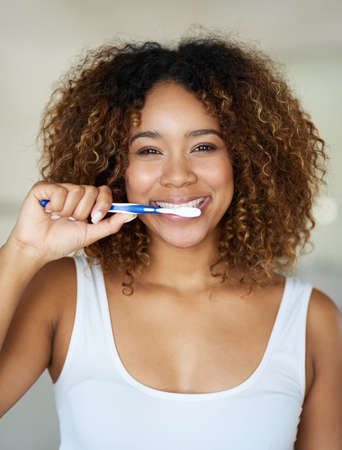 Look after that beautiful smile of yours. Shot of a young woman brushing her teeth in her bathroom.