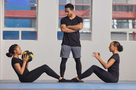 Working out is better with a friend. Shot of two young women exercising with a trainer at the gym.