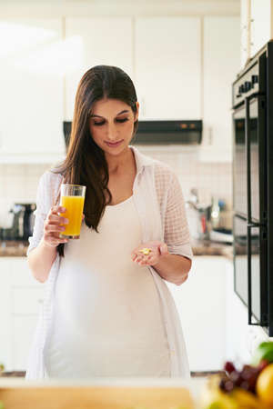 Some vitamin C to go with my vitamins. Shot of a young pregnant woman taking medication with orange juice at home.の写真素材