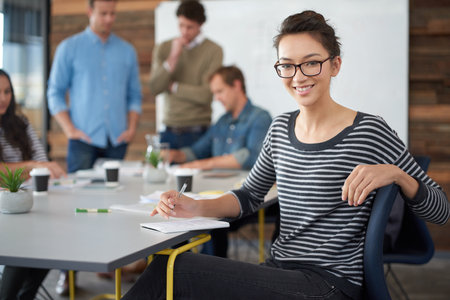 The best office you could hope to work in. Portrait of an attractive young woman sitting in an office with colleagues in the background.の写真素材