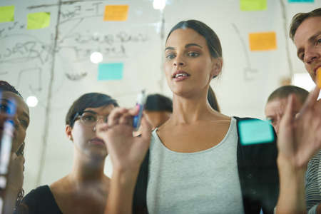 Planning is the first step. Cropped shot of a group of young designers planning on a glass board.の写真素材