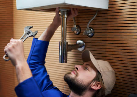 Hes your number one plumber. Shot of a plumber repairing a pipe underneath a sink.の写真素材
