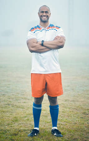 I take pride in my team. Shot of a young sportsman standing on the field during a misty morning.の写真素材
