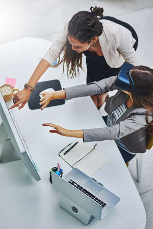 Virtual business. High angle shot of a young businesswoman using a VR headset while being assisted by a female colleague.の写真素材