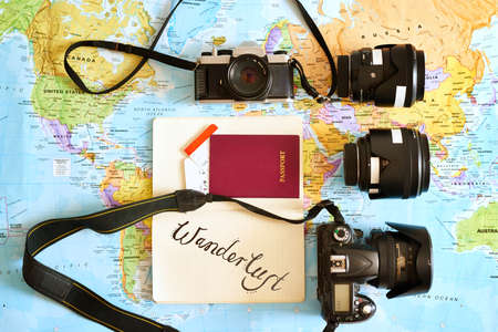 Never travel without your favourite camera. High angle shot of a map with a passport and various cameras and lenses arranged on it.の写真素材