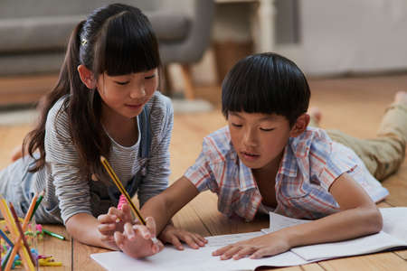 Helping each other with homework. Shot of a cheerful boy and girl doing homework together while lying on the floor at home during the day.の写真素材
