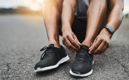 You cant afford to stumble. Closeup shot of a sporty man tying his shoelaces while exercising outdoors.の写真素材