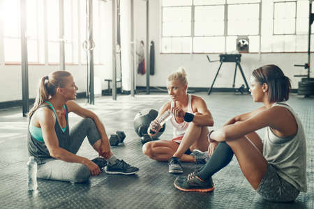 Theyve formed their own fitness squad. Shot of a group of young women taking a break together after a workout at the gym.の写真素材