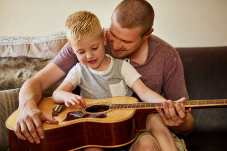 Time for another guitar lesson with Dad. Cropped shot of a father and his little son playing the guitar together at home.の写真素材