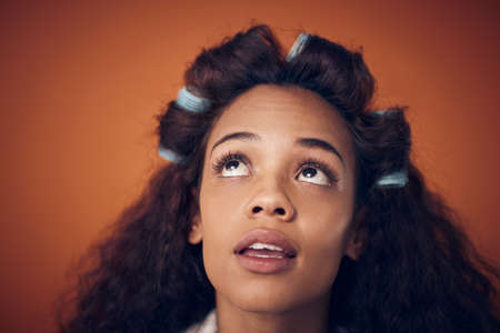 Ill show you how to get perfect curls. Shot of a woman wearing hair rollers while standing against an orange background.の写真素材