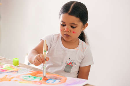 Encourage your children to be creative. Shot of an adorable little girl painting while sitting at a table.の写真素材