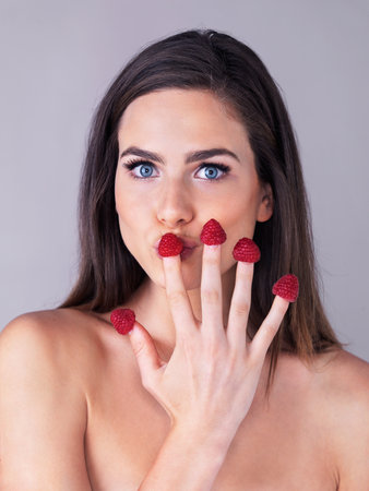 So berry nice. Studio portrait of an attractive young woman eating raspberries off her fingertips against a purple background.の写真素材