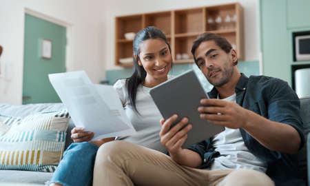Working towards our future one step at a time. Shot of a young couple doing paperwork while using a...