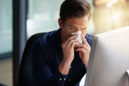 This cold is starting to torture me. Shot of a young businessman blowing his nose in an office.