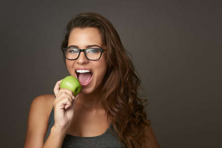 Eating healthy is great for hair, skin and eyesight. Studio shot of a beautiful young woman about to bite an apple against a brown background.の写真素材