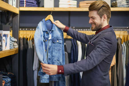 Everyone needs a classic denim jacket in their closet. Shot of a young man looking at clothes in a boutique.の写真素材