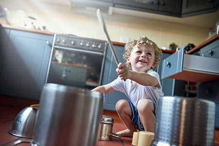 You might call it noise, but kids call it fun. Shot of an adorable little boy playing drums on a set of pots in the kitchen.の写真素材