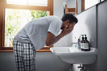Freshening up. Cropped shot of a handsome young man washing his face in the bathroom at home.の写真素材