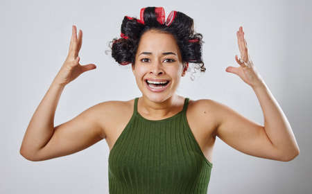 How much longer until I can take this out. Cropped shot of a young woman posing with hair rollers against a grey background.の写真素材