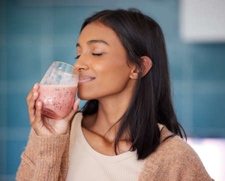 Sipping on a healthy immunity boosting smoothie. Shot of a young woman drinking a healthy smoothie at home.の写真素材