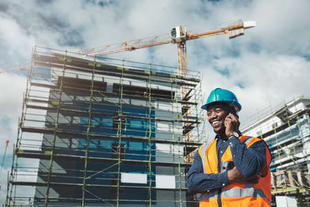 The best building contractor on the block. Shot of a young man using a smartphone while working at a construction site.の写真素材