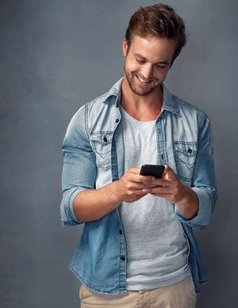 Connected to his friends whenever, wherever. Shot of a happy young man using his smartphone while...