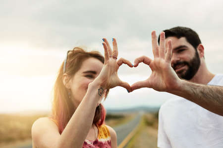 Friends forever. Shot of two young friends putting their hands together to make a heart shape while standing outside next to a road.の写真素材