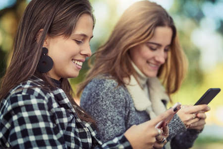 Staying connected, even outside. Cropped shot of two attractive young women using their cellphones...