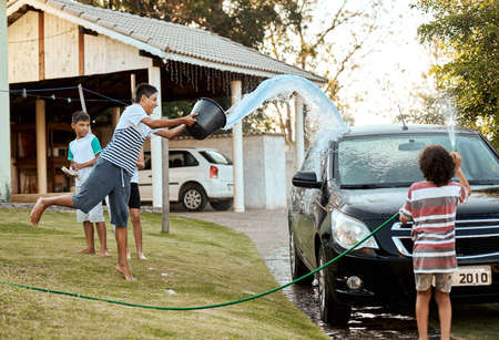 Look out guys Water in coming. Shot of a group of cheerful young kids washing their parents car together outside during the day.の写真素材