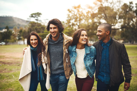 Where are we going to now. Portrait of a group of cheerful young friends huddled together while walking in a park outside during the day.の写真素材