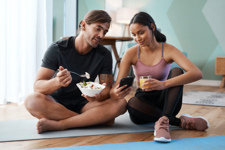 Your diet is just as important as your workout. Full length shot of an athletic young couple enjoying some healthy snacks after their workout at home.の写真素材