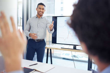 Whats your question. Shot of a young businessman raising his hand to ask a question in a meeting at...