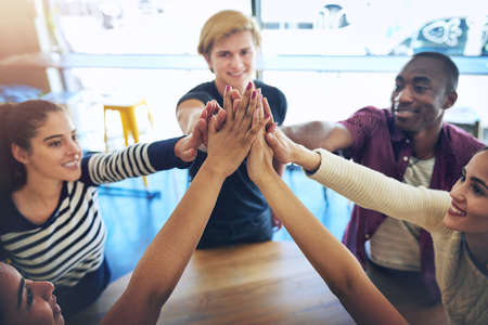 Alone we are smart, together we are brilliant. High angle shot of a group of happy friends high fiving each other.の写真素材