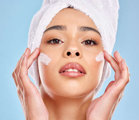 I aint apologising for being fabulous. Studio portrait of an attractive young woman applying moisturiser on her face against a blue background.の写真素材