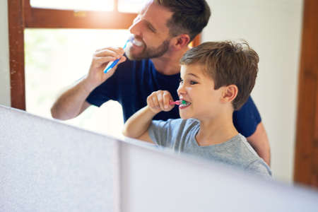 Mine will shine brighter than yours, Dad. Shot of a father and his little son brushing their teeth together at home.の写真素材