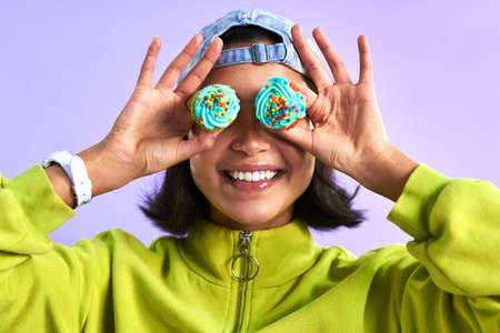 Spread positivity around like sprinkles. Studio shot of a young woman holding cupcakes over her eyes against a purple background.の写真素材