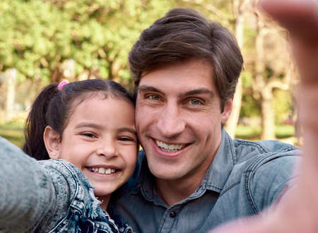 Never forget a single moment. Shot of a happy young man taking a selfie with his adorable daughter in the park.の写真素材