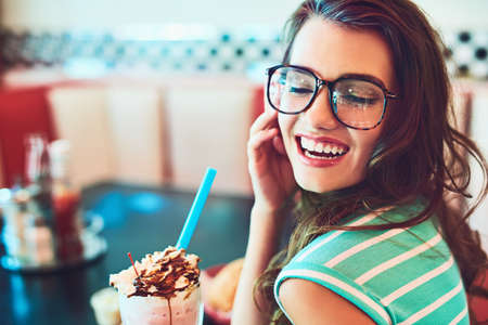In her favourite booth. Cropped shot of an attractive young woman enjoying a milkshake in a retro diner.の写真素材