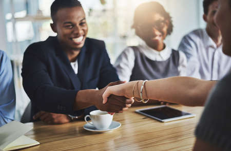 Its a deal. Cropped shot of two young businesspeople shaking hands during a meeting in the...