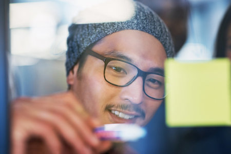 He knows how to bring his visions to life. Shot of a young businessman brainstorming with notes on a glass wall in an office.の写真素材
