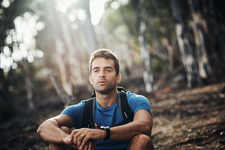 Its just me and my thoughts. Cropped shot of a carefree young man taking a quick break from hiking up a mountain during the day.の写真素材